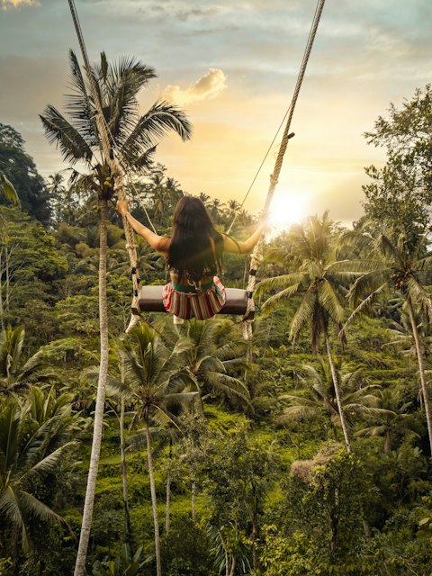 Mulher num balanço entre palmeiras ao pôr do sol, em Bali